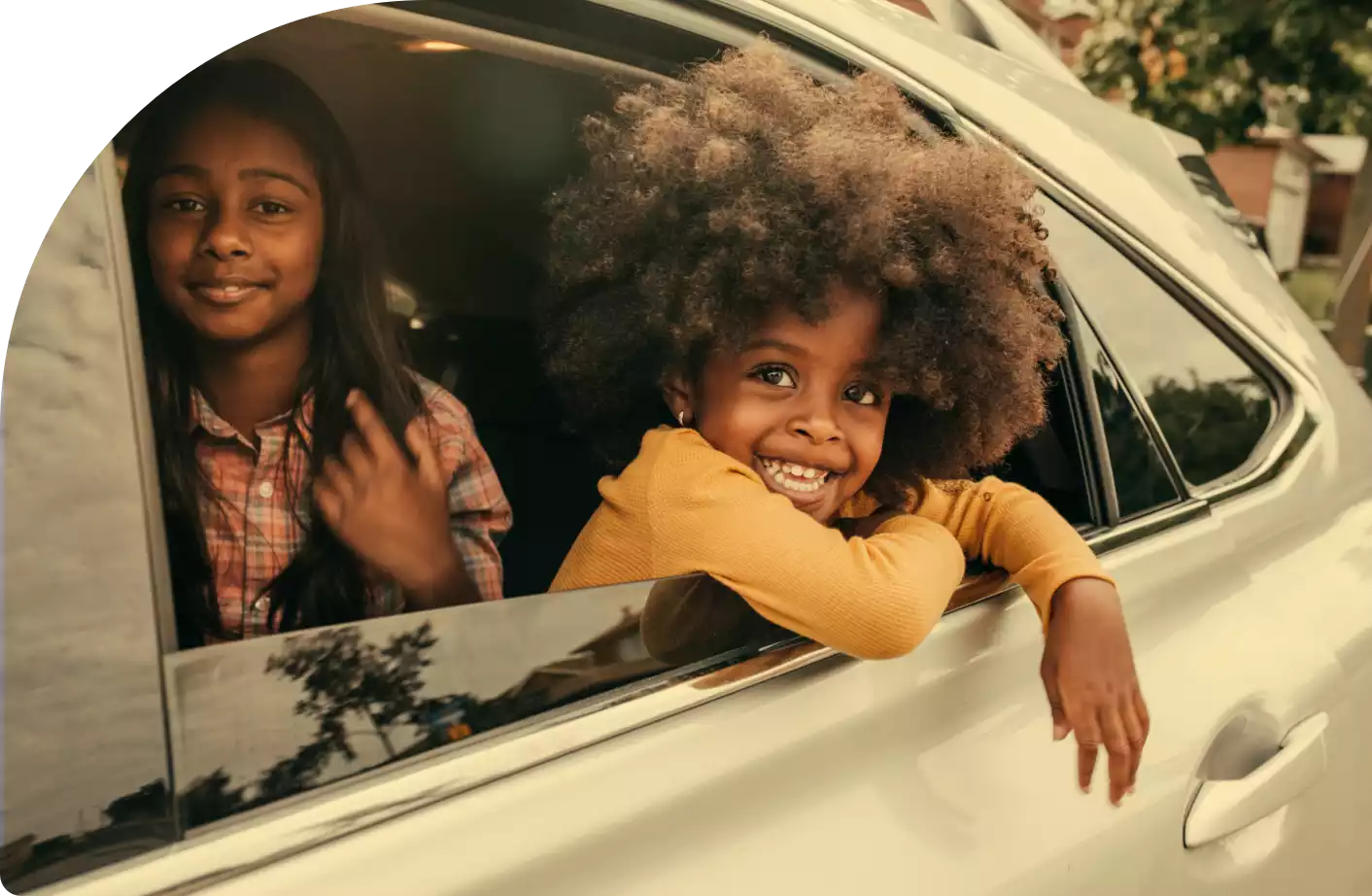 Two happy young girls in backseat of car, looking out window