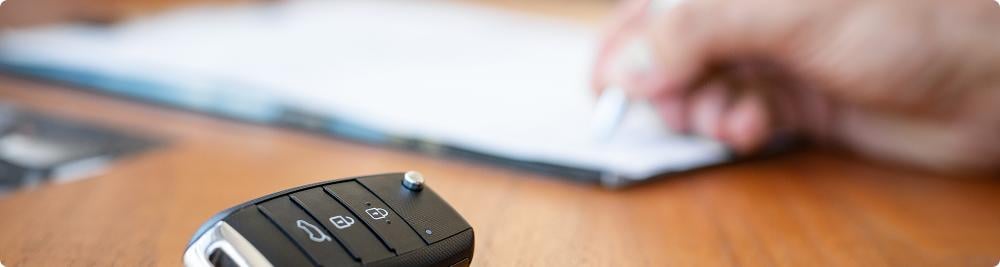 car key fob next to hand signing paperwork