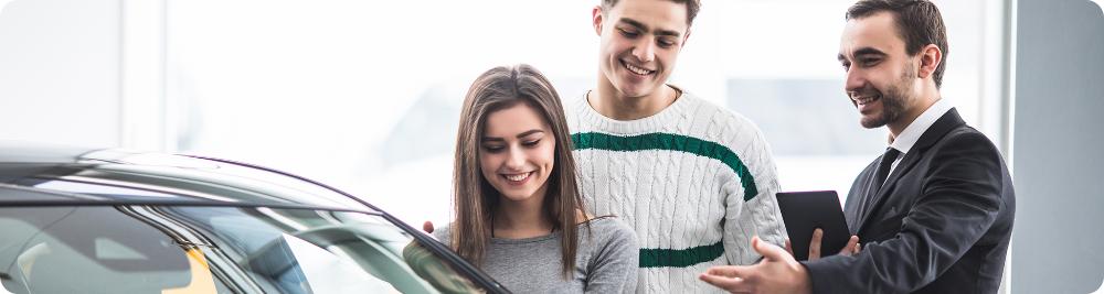 couple speaks to dealer in front of new car