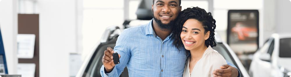 happy couple hold car keys in front of new car