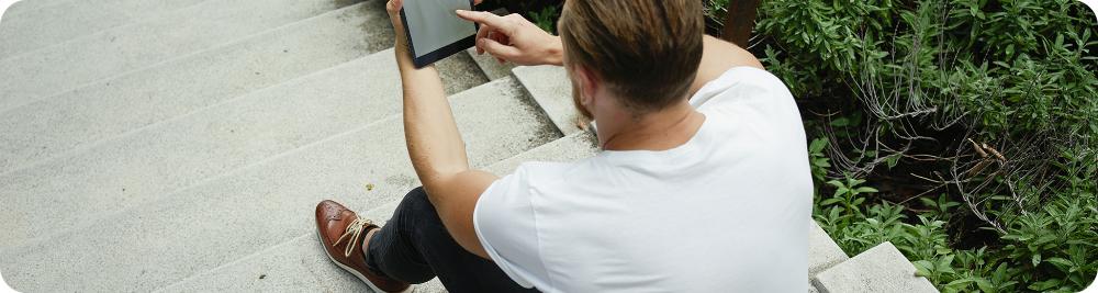 young man uses tablet sitting outside